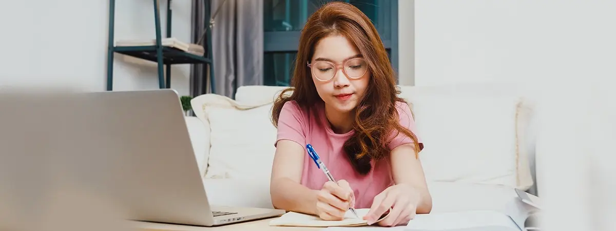 A student is taking notes during her online class.